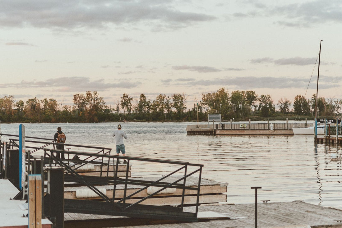 Two anglers fishing from a dock beside a calm lake at sunset