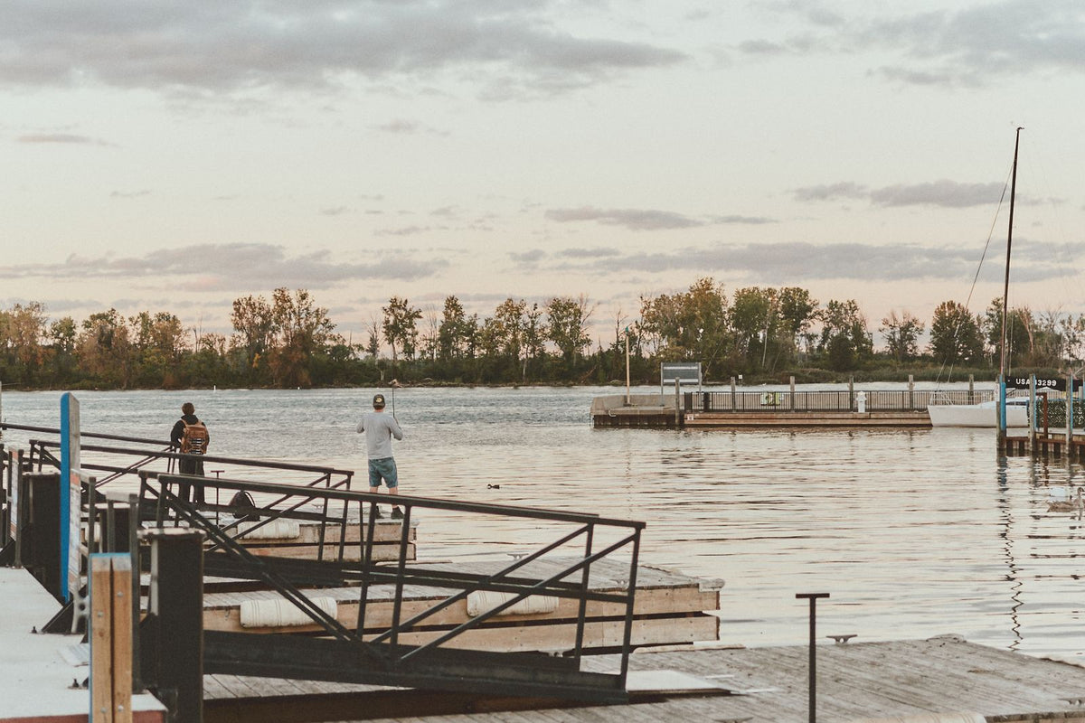 Two anglers fishing from a dock beside a calm lake at sunset
