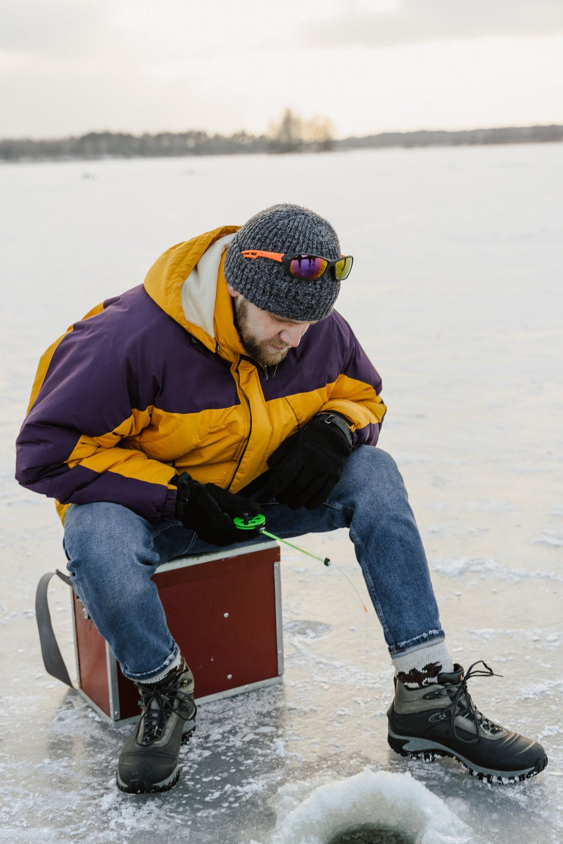 Angler in winter clothes fishing beside a hole in a frozen lake