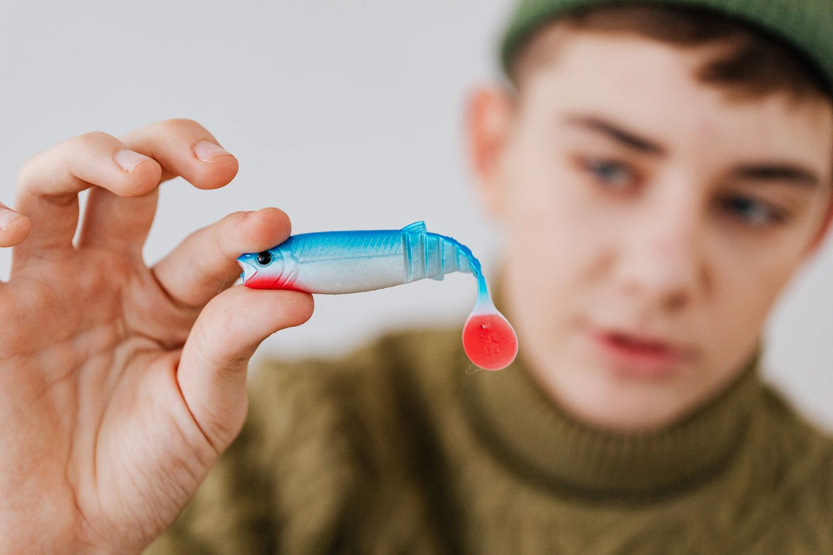 Person holding a blue and red soft plastic paddle-tail lure close to the camera